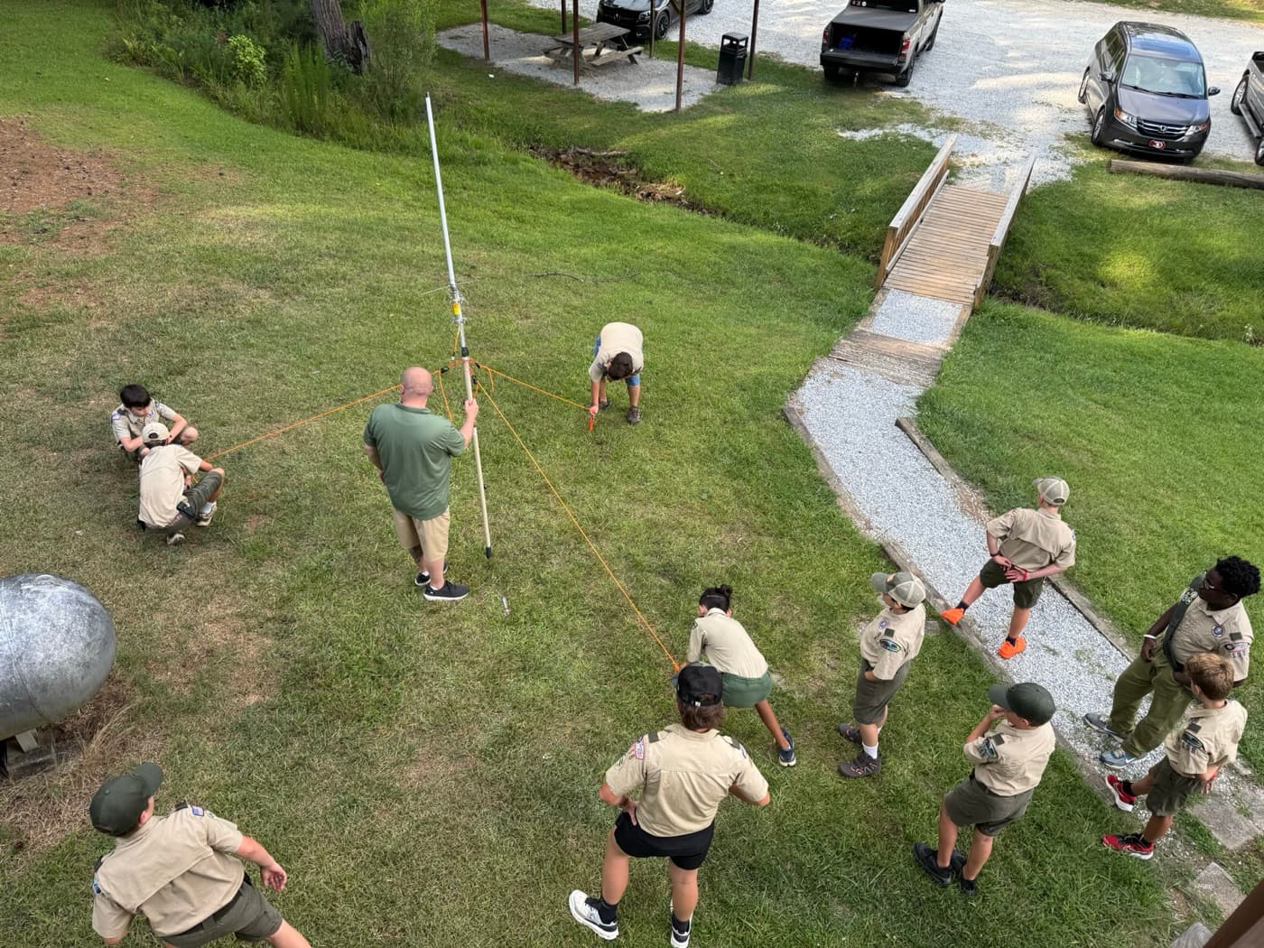 Scouts and Chris raising a portable vertical antenna with guy lines on a grassy field